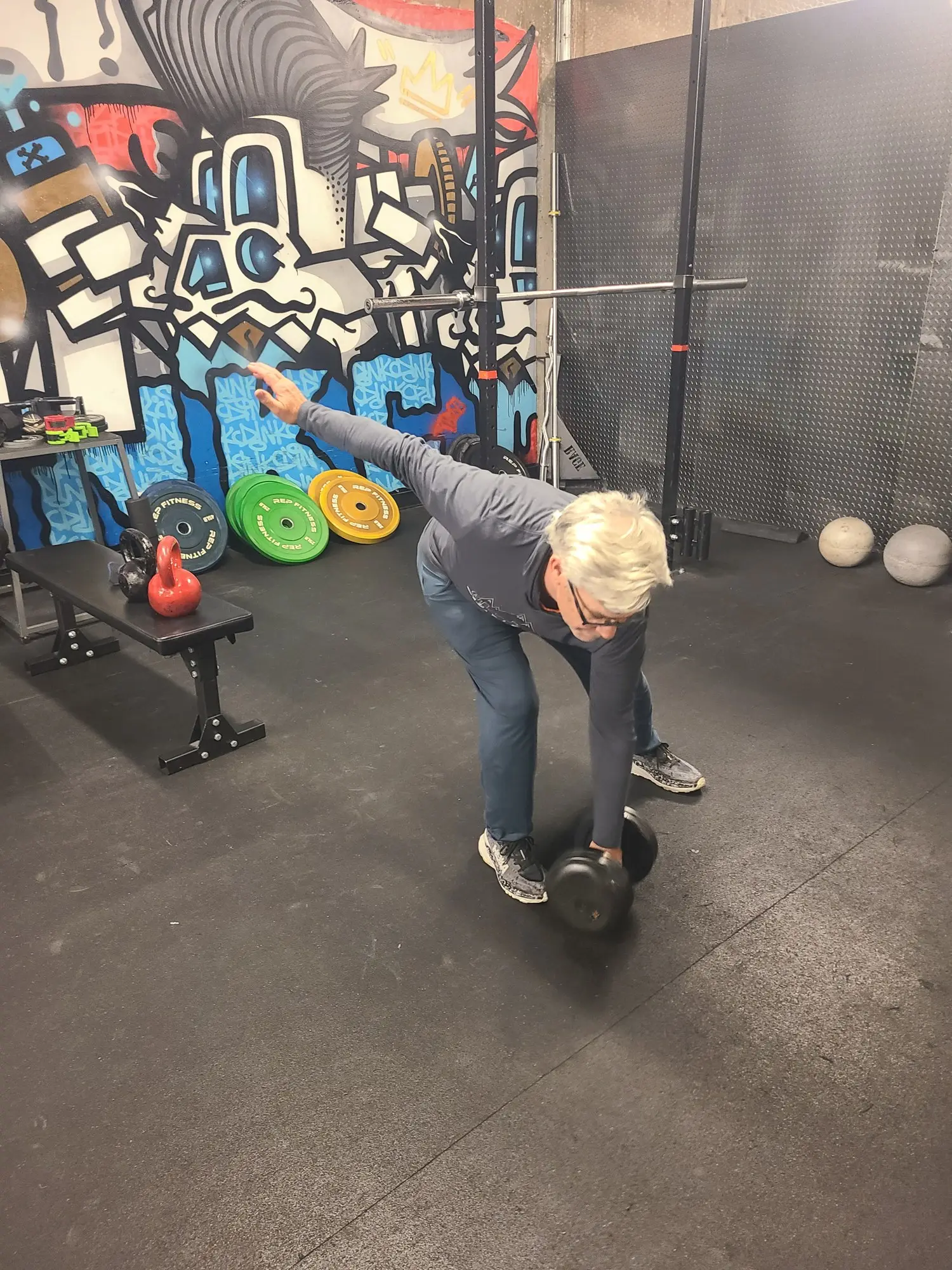 A client in his sixties hinging with a kettlebell in front of the mural at the Denver studio