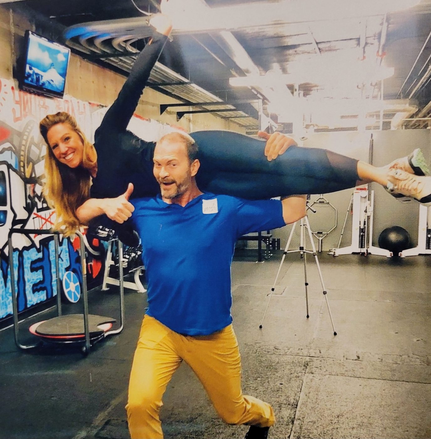 Jamie Atlas lifting a smiling client across his shoulders in the studio